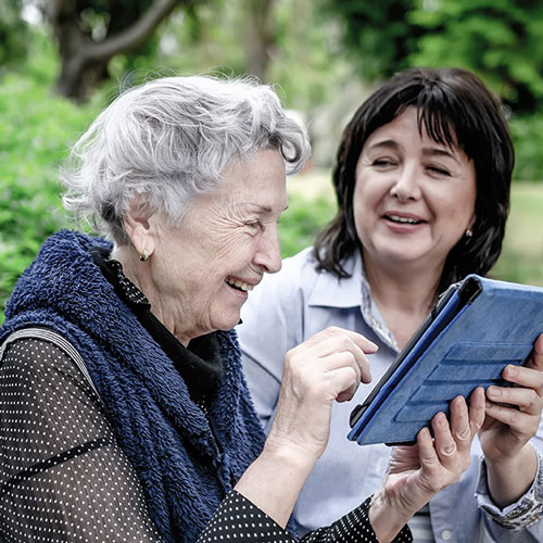 Middle-aged woman helping an eldery woman use a tablet