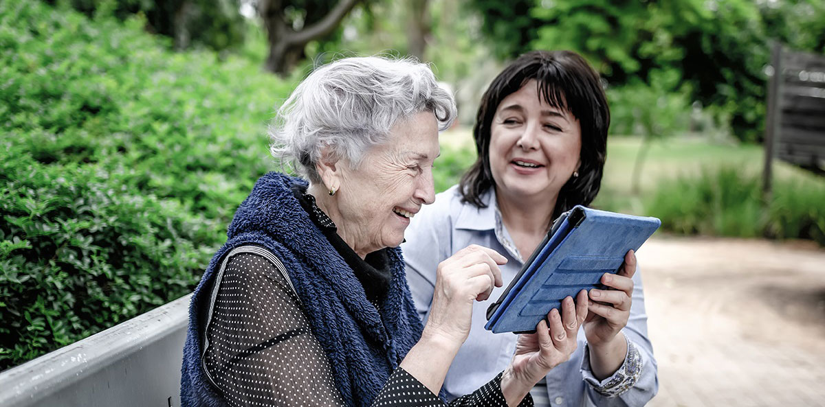 Middle-aged woman helping an eldery woman use a tablet