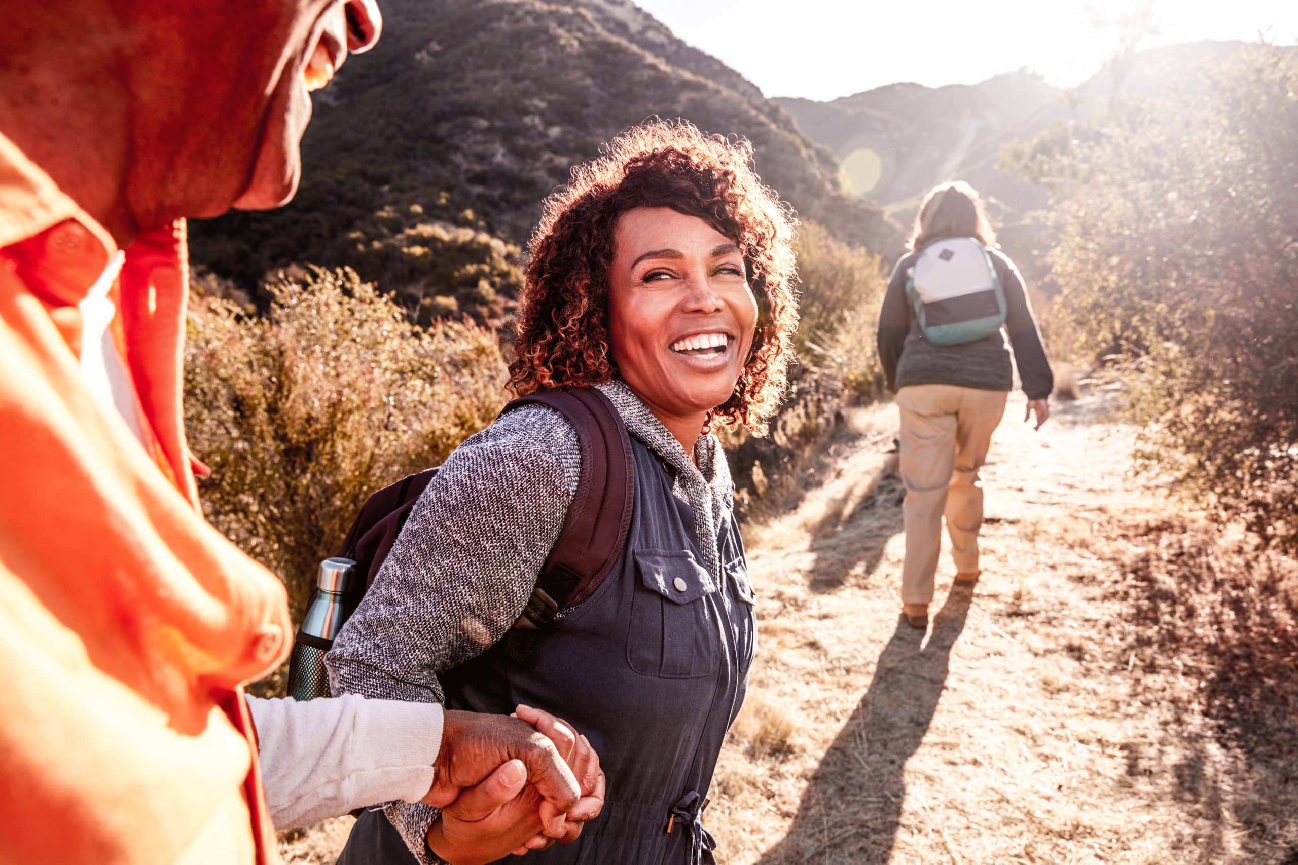 Woman Helping Man On Trail As Group Of Senior Friends Go Hiking In Countryside Together