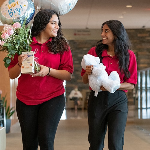 Two young volunteers (in their red NGHS Auxiliary polos) on their way to deliver balloons and a teddy bear to a new parent in the hospital.