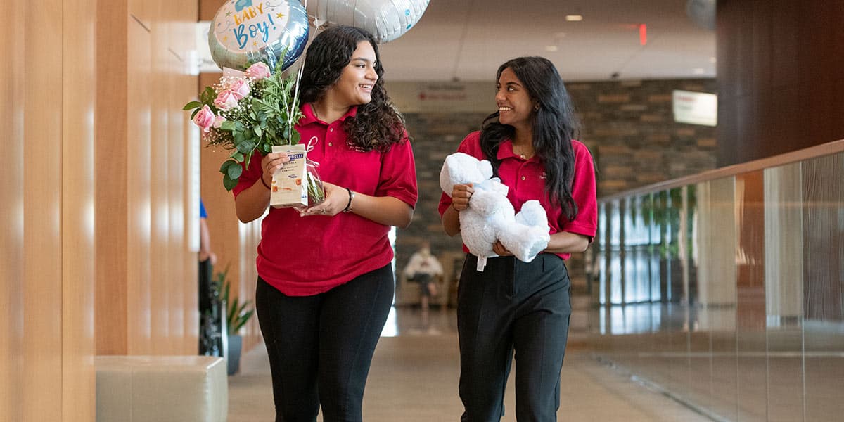 Two young volunteers (in their red NGHS Auxiliary polos) on their way to deliver balloons and a teddy bear to a new parent in the hospital.