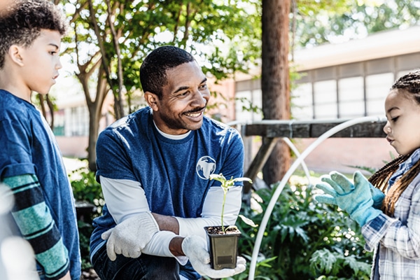 At the school garden, the mid adult male community outreach volunteer teaches children gardening.
