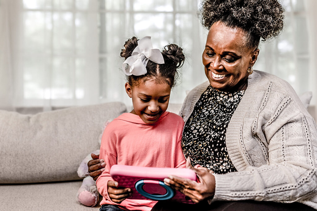Grandmother sitting with granddaughter looking at tablet.