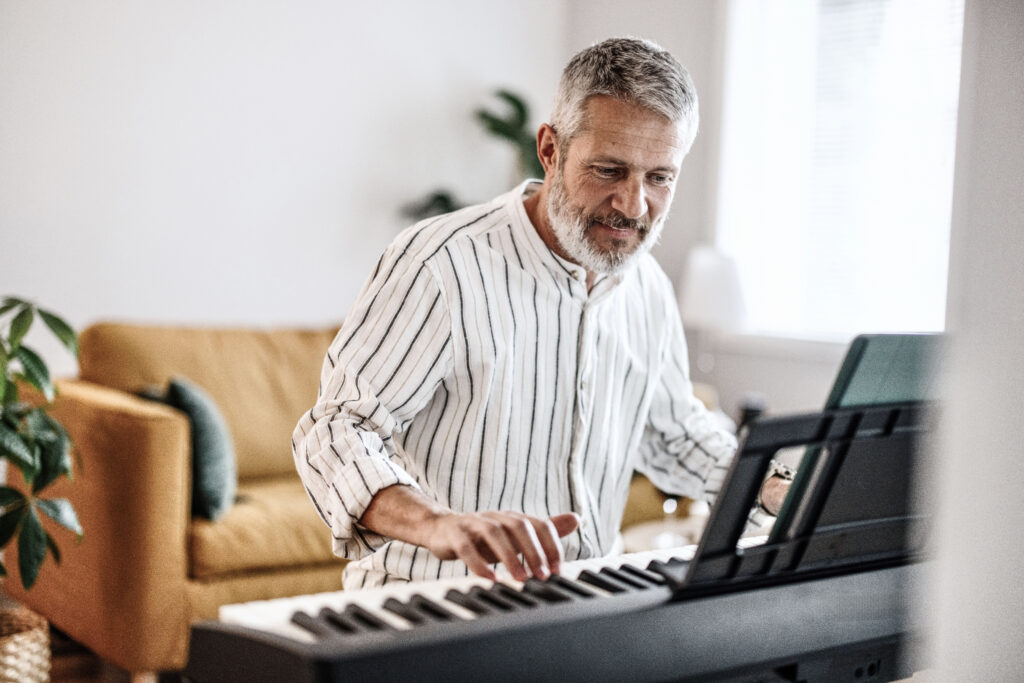 Happy man plays piano in well lit living room with orange couch in background.