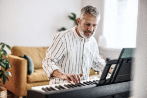 Happy man plays piano in well lit living room with orange couch in background.