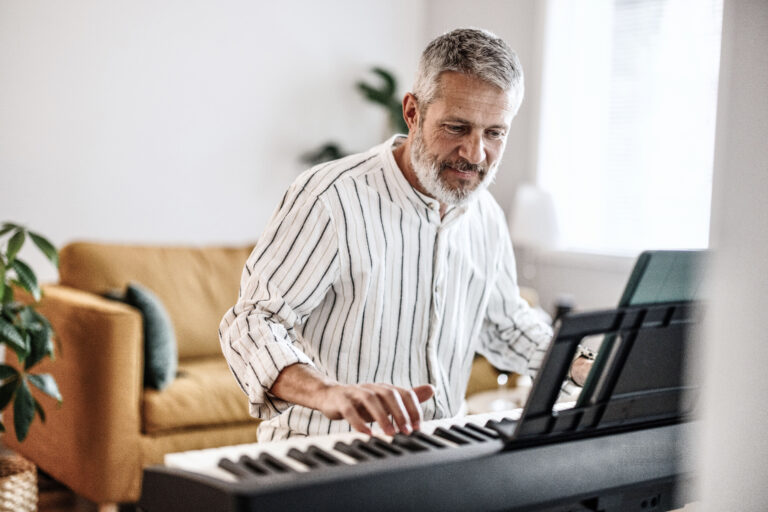 Happy man plays piano in well lit living room with orange couch in background.