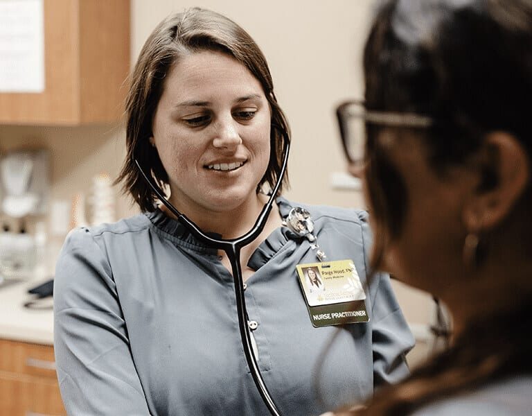 Nurse practitioner using a stethoscope to examine a patient in a medical office.