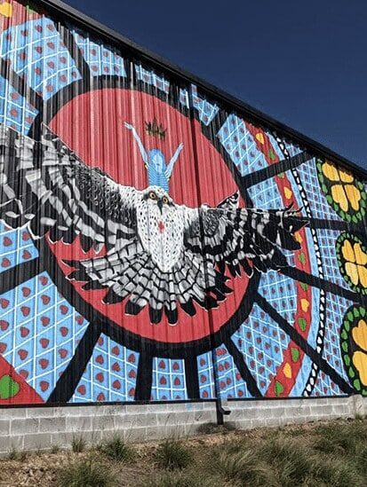 Colorful outdoor mural featuring a large owl with outstretched wings against a patterned background