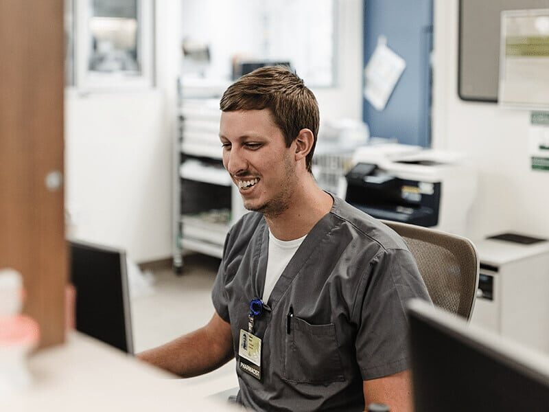Healthcare professional in gray scrubs working at a computer in a clinical office.