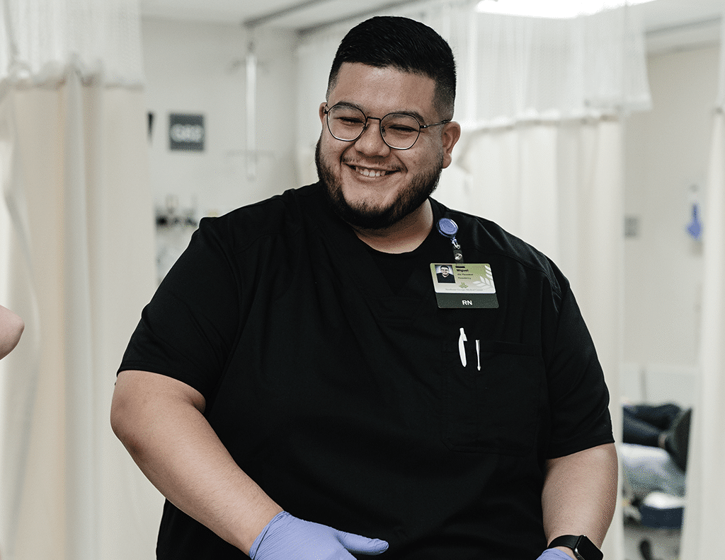Smiling nurse in black scrubs with RN badge assisting a patient in a hospital room