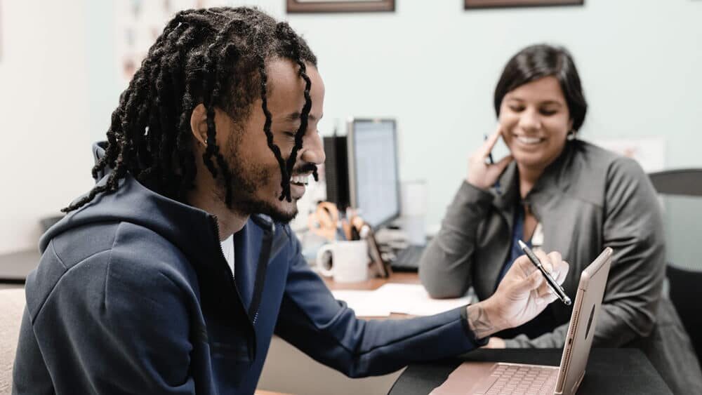 Two colleagues smiling while reviewing information on a tablet in an office setting